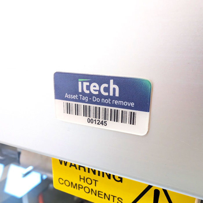 Itech asset tag with barcode and serial number 001245 on a metal surface, with a yellow warning label below reading 'HOT COMPONENTS'.