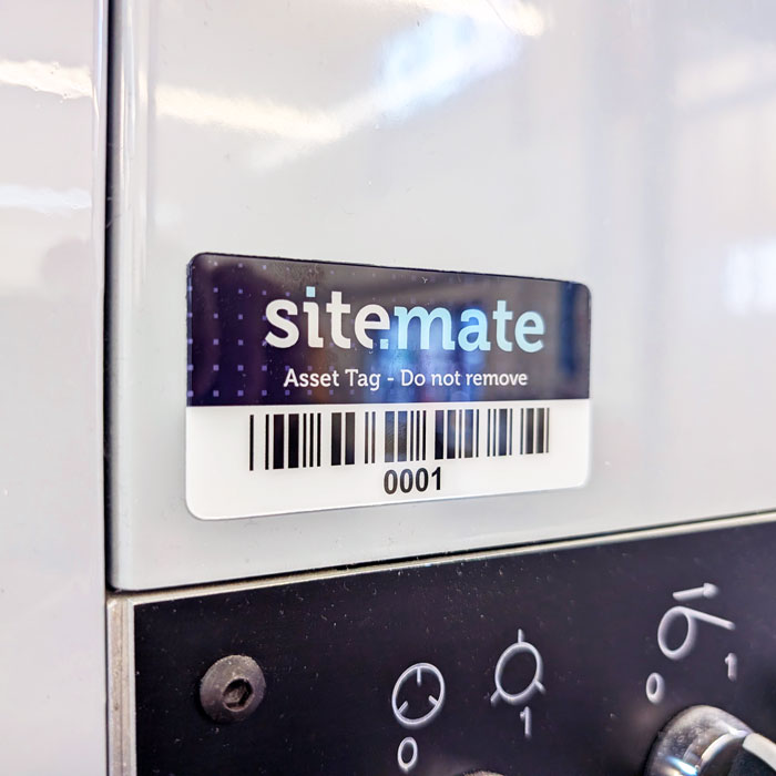 Asset tag on a metal surface: 'sitemate' with a barcode and ID 0001 (Do not remove).