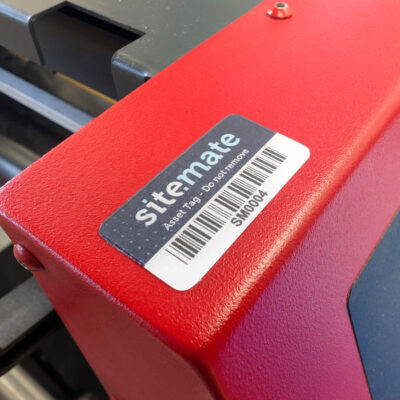 Close‑up of red industrial equipment with a SiteMATE asset tag and barcode reading SM004 (Do not remove).