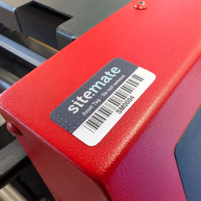 Close‑up of red industrial equipment with a SiteMATE asset tag and barcode reading SM004 (Do not remove).
